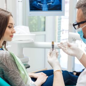 Male dentist showing his female patient a dental implant in clinic
